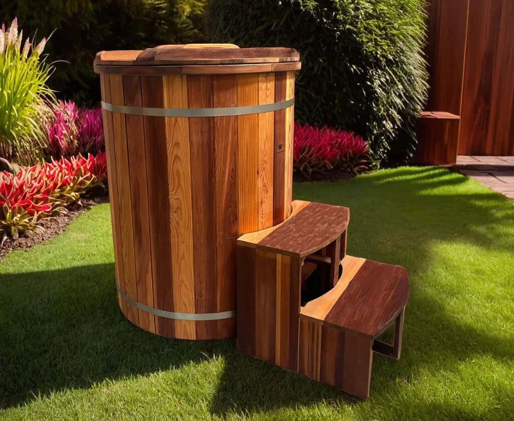 The Artisan Barrel Ice Bath with Chiller, crafted from treated cedar, set in a lush garden with vibrant flowers.