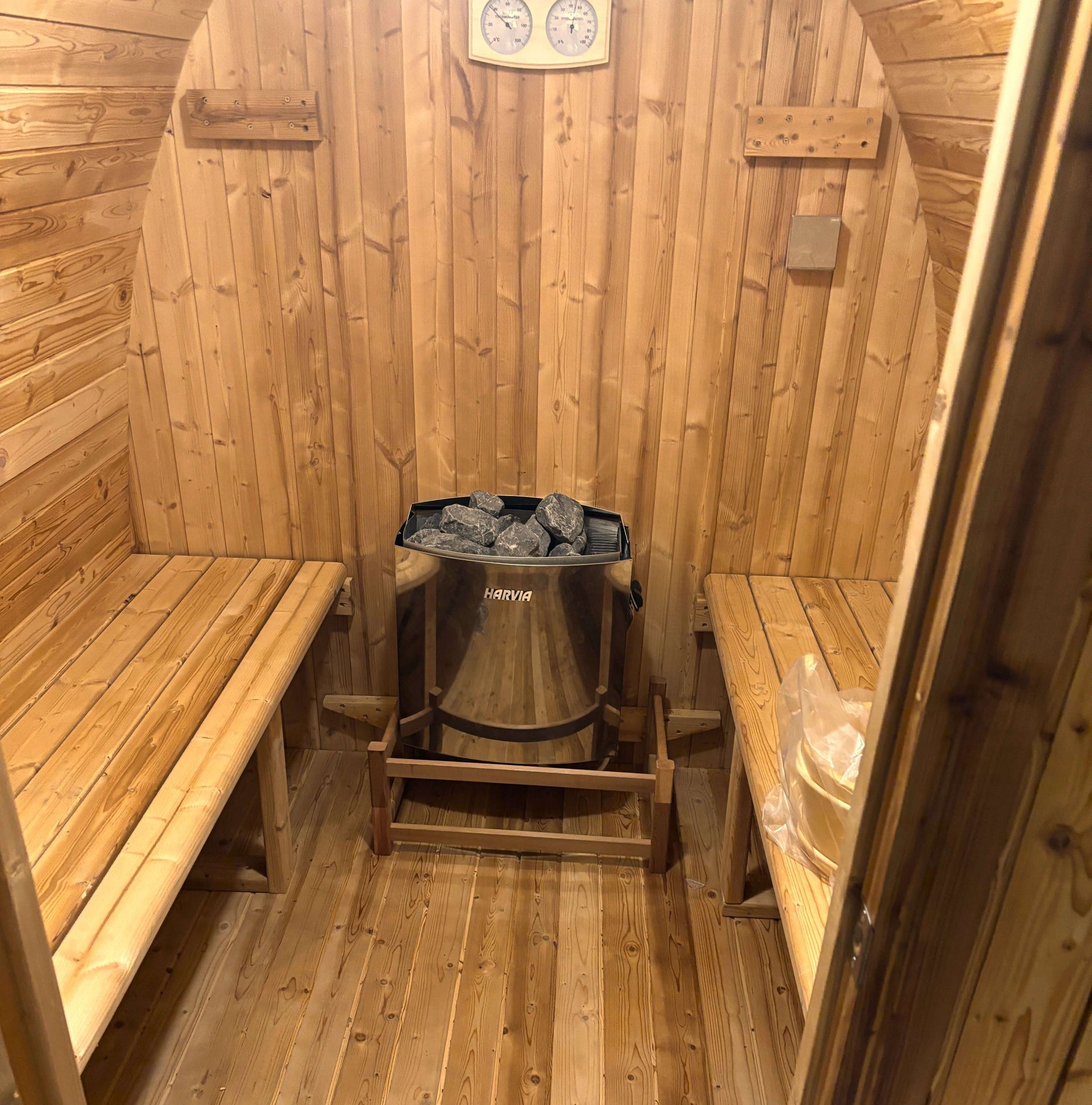 Interior view of a sauna featuring wooden benches and a Harvia heater with stones.